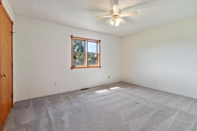 spare room featuring light carpet, ceiling fan, and a textured ceiling