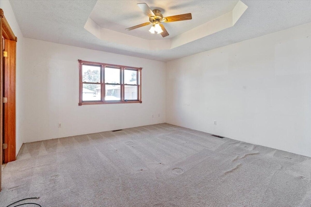 carpeted spare room with ceiling fan and a tray ceiling