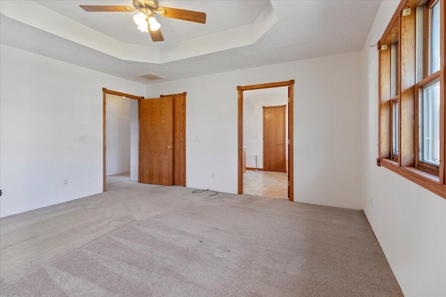 carpeted empty room with ceiling fan and a tray ceiling