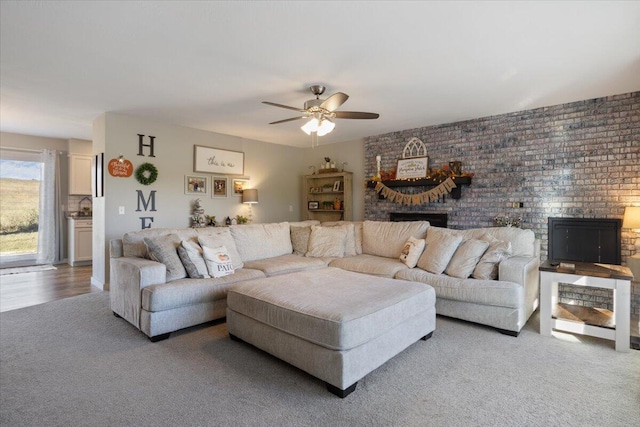 living room with ceiling fan, brick wall, a brick fireplace, and hardwood / wood-style floors