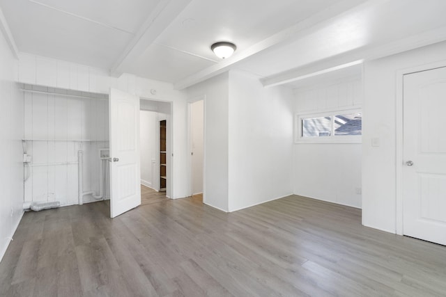 unfurnished bedroom with beam ceiling and light hardwood / wood-style floors