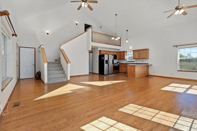 unfurnished living room with visible vents, a ceiling fan, stairs, light wood-style flooring, and high vaulted ceiling