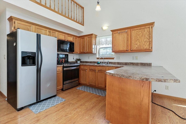 kitchen with stainless steel appliances, sink, decorative light fixtures, light hardwood / wood-style floors, and kitchen peninsula