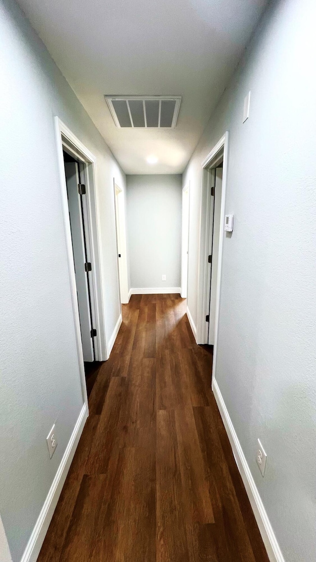 hallway with baseboards, wood finished floors, and visible vents