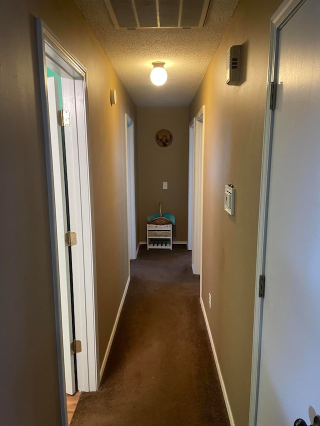 hallway featuring dark colored carpet and a textured ceiling