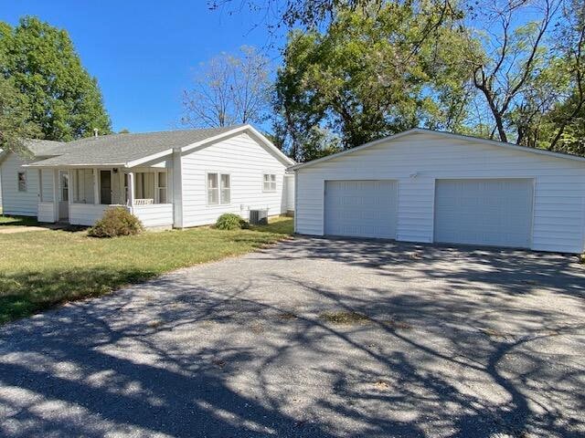 ranch-style house with an outbuilding, a porch, a front yard, a garage, and cooling unit