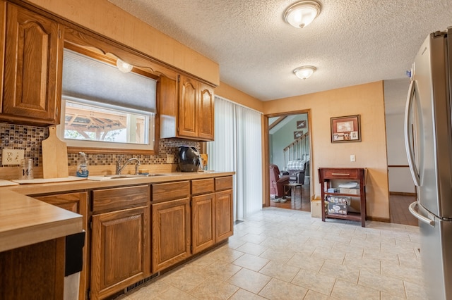 kitchen featuring stainless steel refrigerator, backsplash, sink, and a textured ceiling