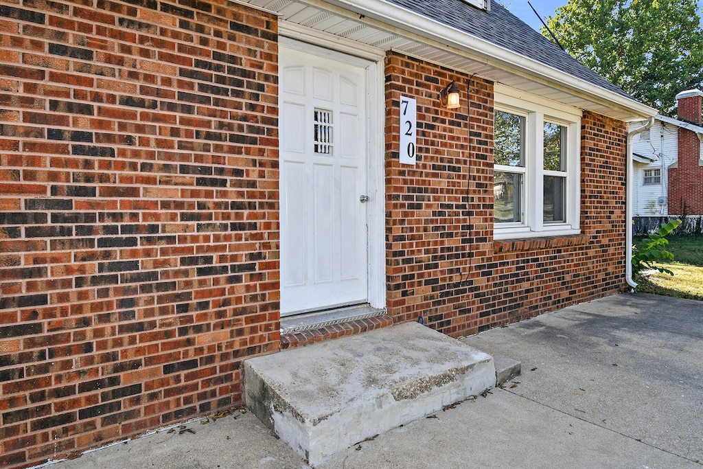 doorway to property with a shingled roof and brick siding