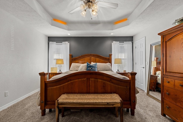 carpeted bedroom with a raised ceiling, a textured ceiling, and ceiling fan