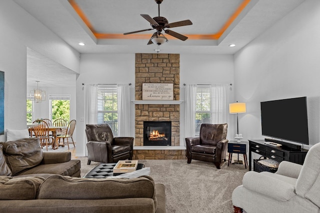 living room with a raised ceiling, ceiling fan with notable chandelier, a high ceiling, a fireplace, and carpet floors