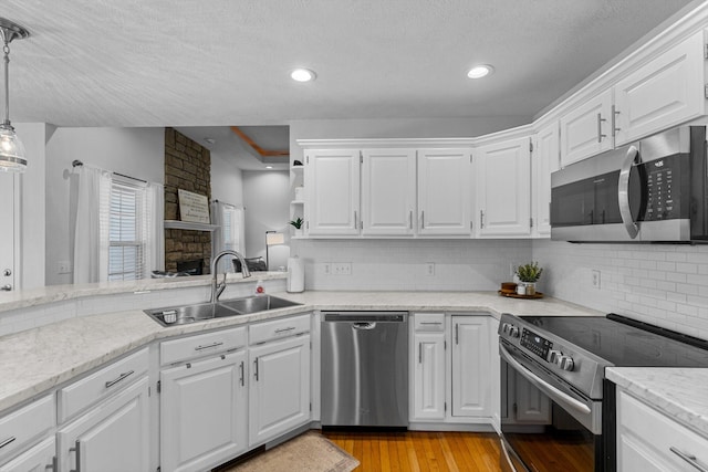 kitchen featuring light wood-type flooring, stainless steel appliances, sink, hanging light fixtures, and white cabinetry