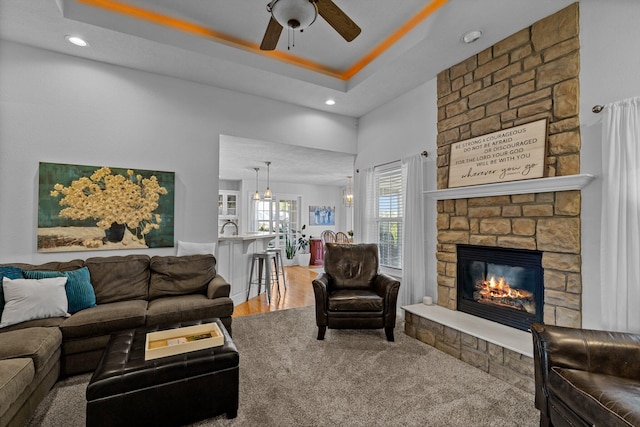 living room featuring a raised ceiling, ceiling fan, hardwood / wood-style flooring, and a stone fireplace