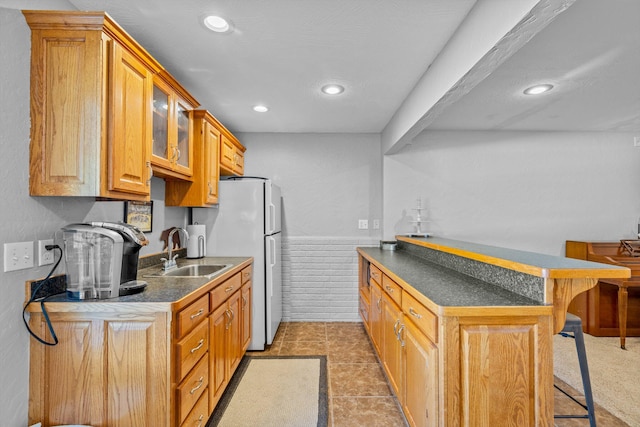 kitchen with white refrigerator, dark tile patterned flooring, a breakfast bar, sink, and kitchen peninsula