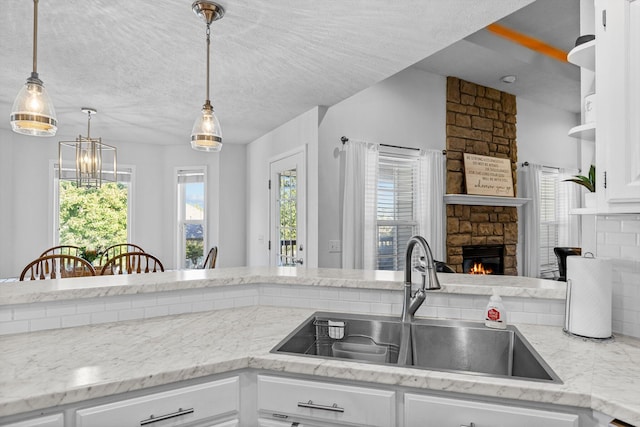 kitchen with a stone fireplace, pendant lighting, sink, and white cabinetry