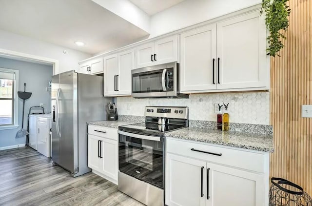 kitchen with washing machine and dryer, appliances with stainless steel finishes, light wood-type flooring, and white cabinetry