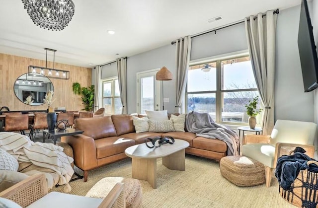 living room featuring light carpet, an inviting chandelier, wooden walls, and a healthy amount of sunlight