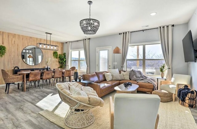 living room with an inviting chandelier, light hardwood / wood-style flooring, wooden walls, and a healthy amount of sunlight