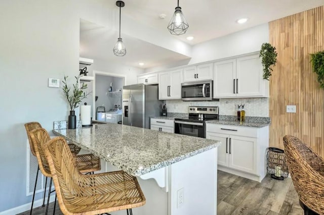 kitchen featuring white cabinets, hanging light fixtures, kitchen peninsula, stainless steel appliances, and a kitchen breakfast bar