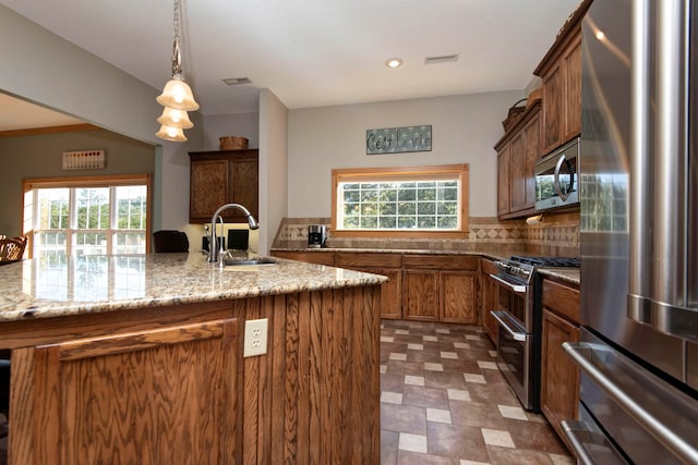 kitchen with appliances with stainless steel finishes, pendant lighting, light stone counters, and sink