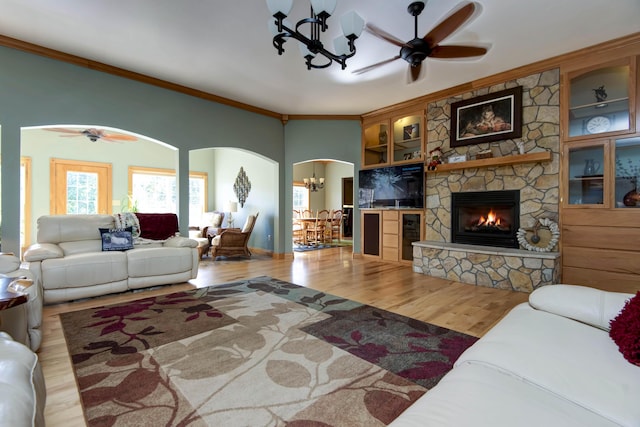 living room featuring built in features, ceiling fan with notable chandelier, light hardwood / wood-style flooring, a fireplace, and ornamental molding