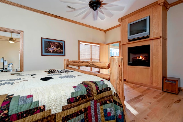 bedroom with a large fireplace, ornamental molding, light hardwood / wood-style flooring, and ceiling fan