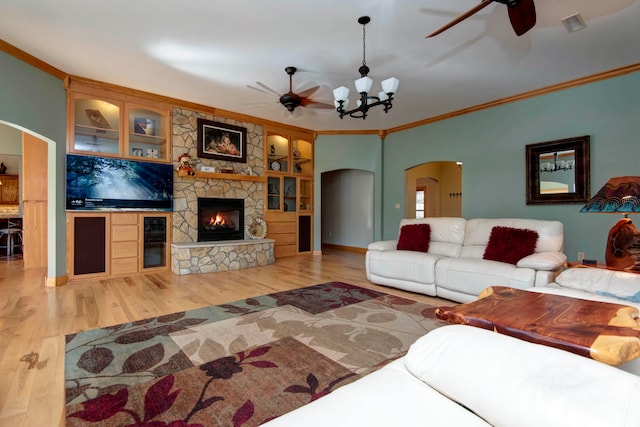 living room featuring ceiling fan with notable chandelier, ornamental molding, light wood-type flooring, and a stone fireplace