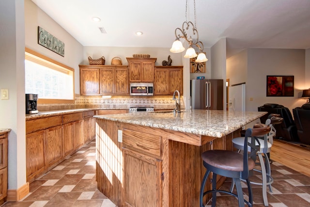 kitchen with a chandelier, backsplash, sink, stainless steel appliances, and an island with sink