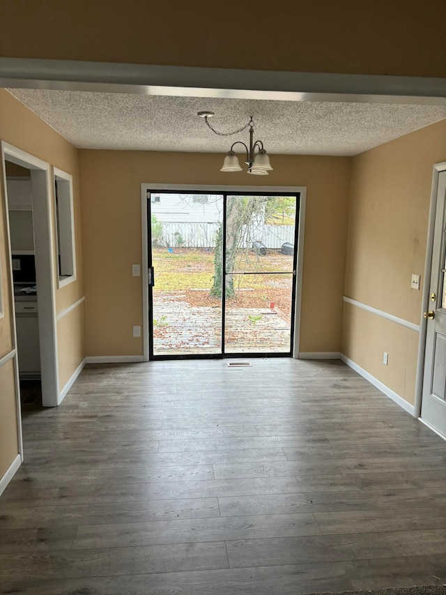 unfurnished dining area with an inviting chandelier, hardwood / wood-style flooring, and a textured ceiling