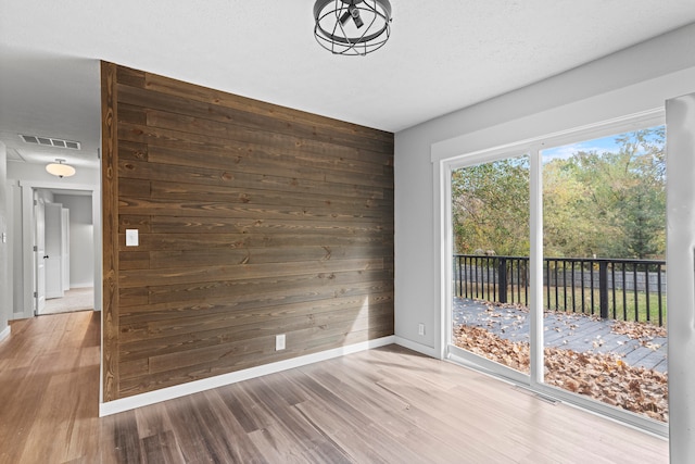 spare room featuring wood walls, a textured ceiling, and hardwood / wood-style floors