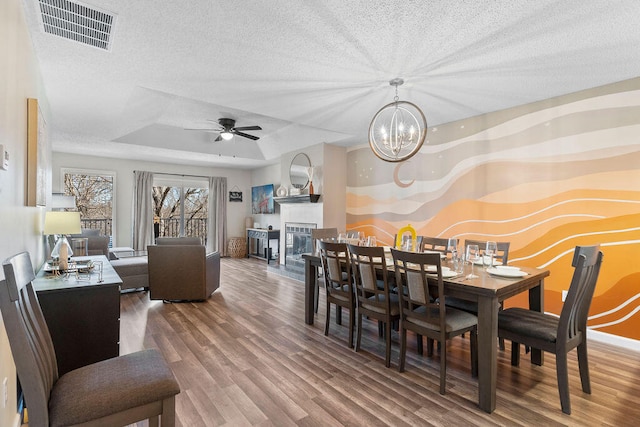 dining space with wood-type flooring, a textured ceiling, ceiling fan with notable chandelier, and a raised ceiling