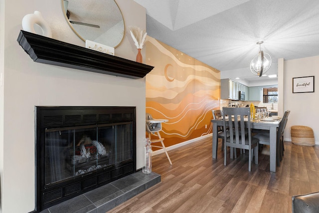 dining room with wood-type flooring, an inviting chandelier, a tiled fireplace, and a textured ceiling