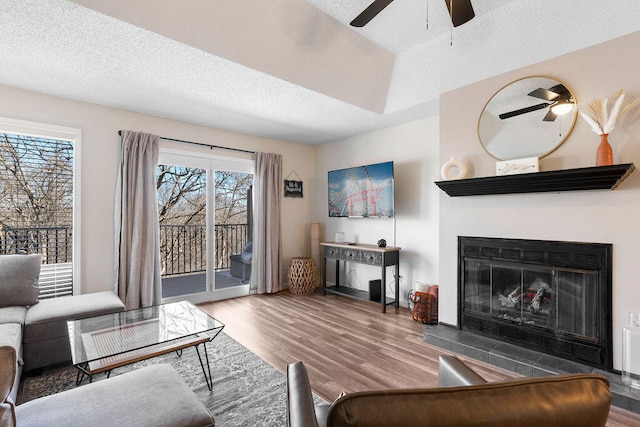 living room featuring wood-type flooring, a textured ceiling, a fireplace, and ceiling fan