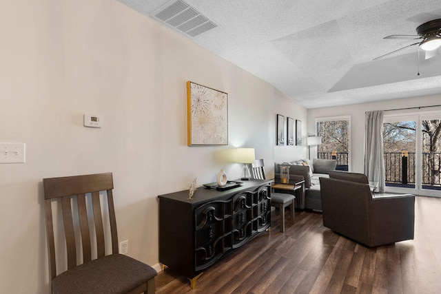 living room featuring dark wood-type flooring, ceiling fan, and a textured ceiling