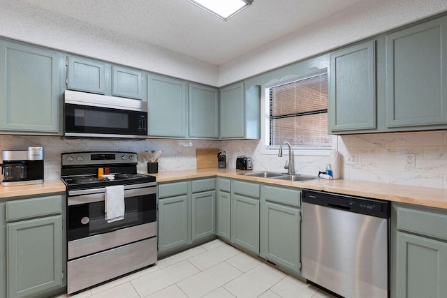 kitchen with sink, stainless steel appliances, backsplash, light tile patterned floors, and a textured ceiling