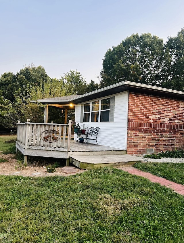 rear view of house featuring a wooden deck, a lawn, and brick siding