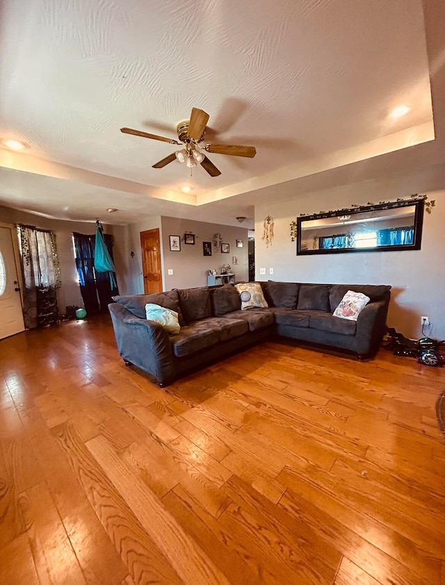 unfurnished living room with a tray ceiling, ceiling fan, and wood-type flooring