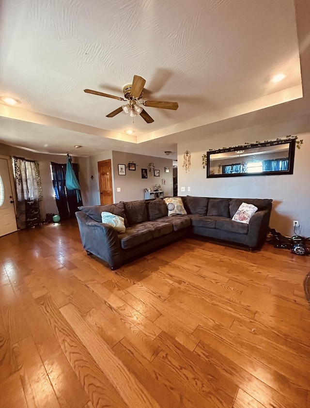living area featuring light wood finished floors, a ceiling fan, and a tray ceiling