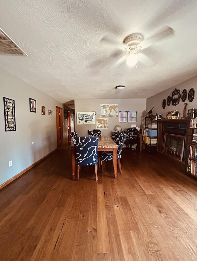 dining room featuring a ceiling fan, wood finished floors, a textured ceiling, and a fireplace