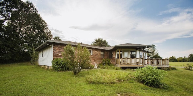 rear view of property featuring a lawn, brick siding, and a deck