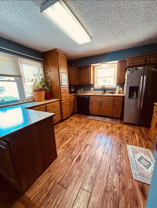 kitchen featuring black dishwasher, a healthy amount of sunlight, stainless steel refrigerator with ice dispenser, and light hardwood / wood-style floors