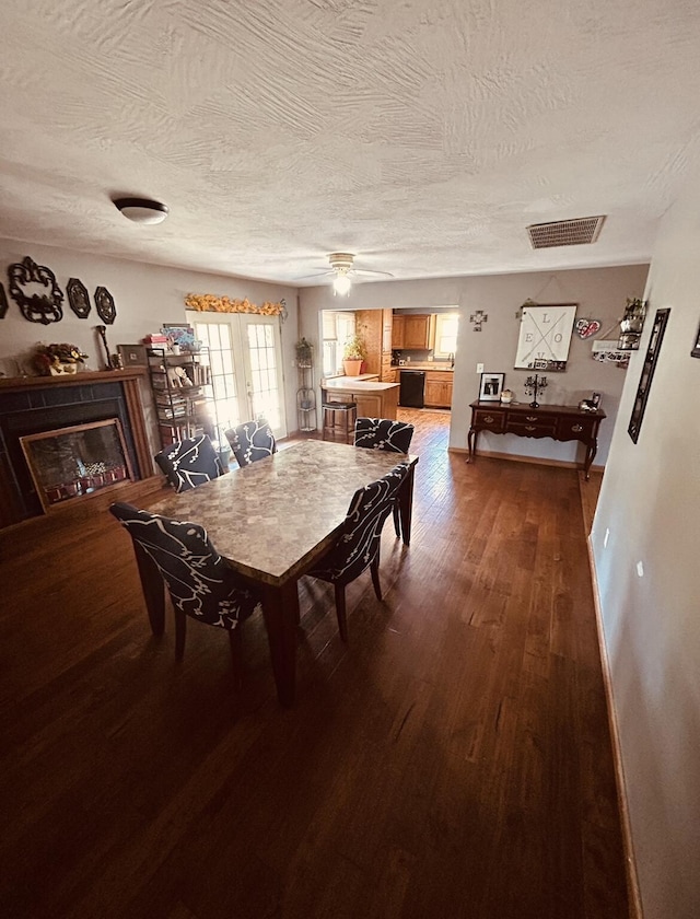 dining room with a glass covered fireplace, visible vents, a textured ceiling, and dark wood-type flooring
