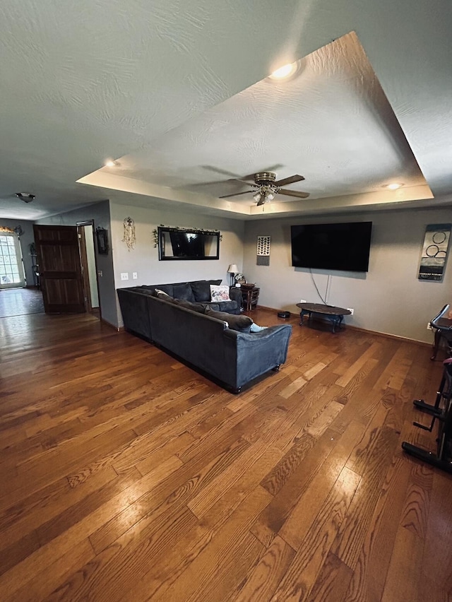 living area featuring a tray ceiling, hardwood / wood-style floors, baseboards, and ceiling fan