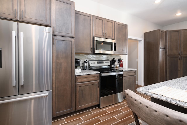 kitchen with light stone counters, appliances with stainless steel finishes, dark hardwood / wood-style floors, and decorative backsplash