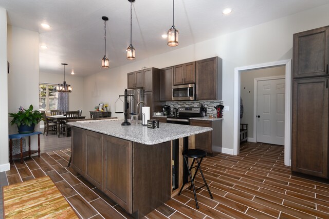 kitchen featuring dark brown cabinetry, pendant lighting, an island with sink, dark wood-type flooring, and appliances with stainless steel finishes