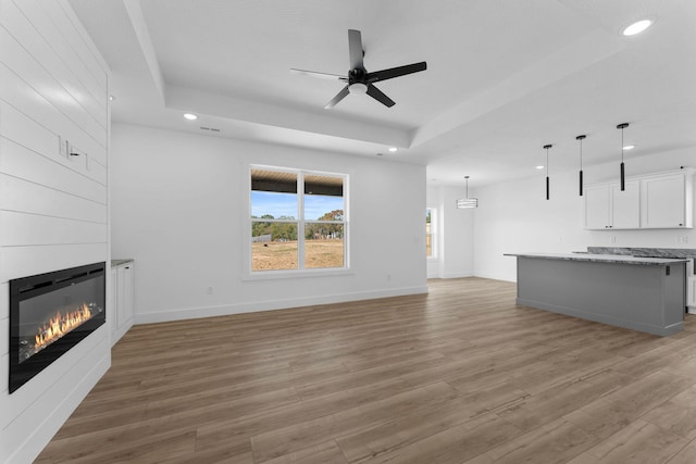 unfurnished living room with a fireplace, a tray ceiling, and light hardwood / wood-style floors