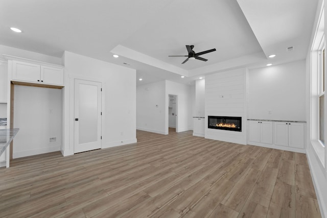 unfurnished living room featuring a fireplace, ceiling fan, a tray ceiling, and light hardwood / wood-style flooring