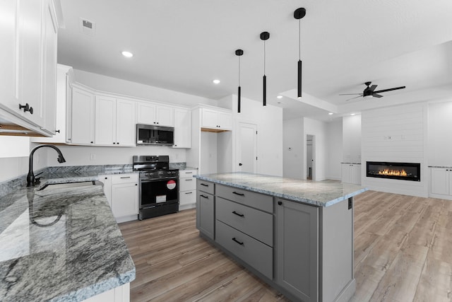 kitchen with light hardwood / wood-style floors, a kitchen island, black gas range, sink, and white cabinets