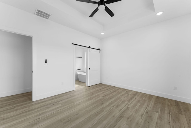 unfurnished bedroom featuring a barn door, ceiling fan, light hardwood / wood-style flooring, and ensuite bath