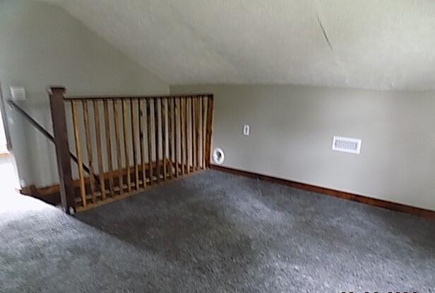 additional living space featuring dark colored carpet and vaulted ceiling