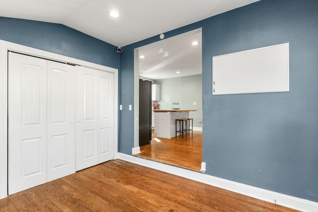 unfurnished bedroom with wood-type flooring, a closet, and vaulted ceiling